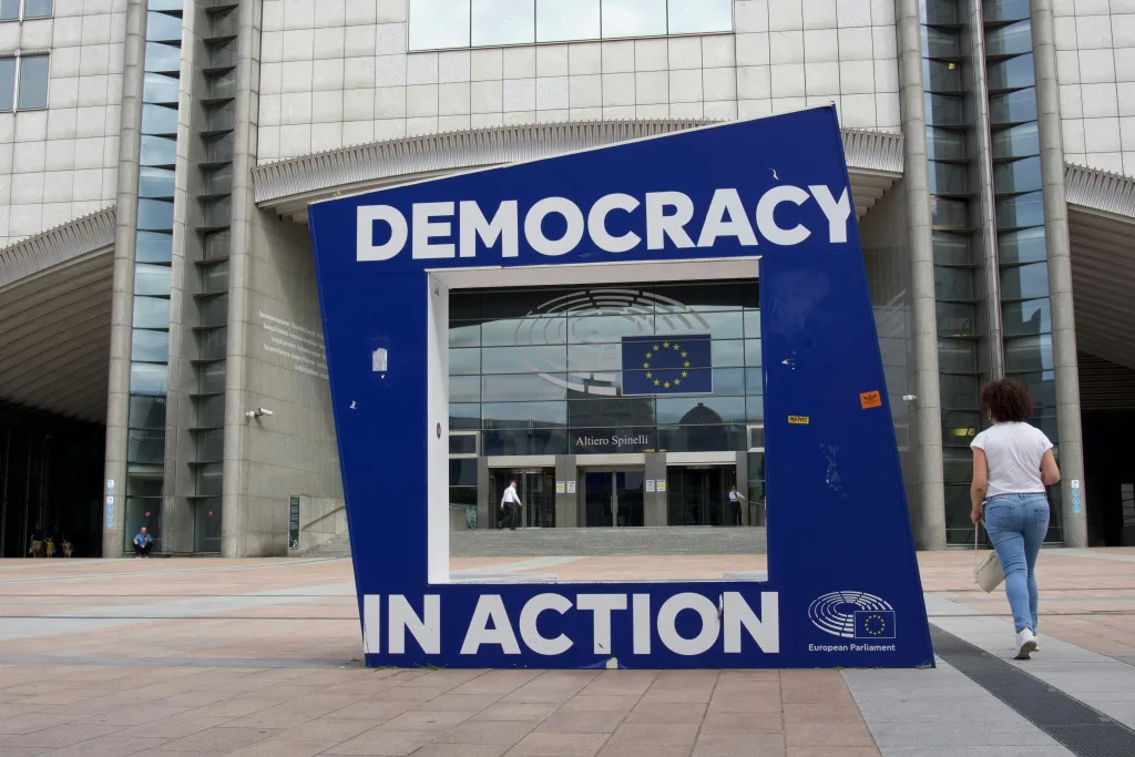 Entrance of European Union Parliament in Brussels, Belgium. Installation of a blue frame in front, showing the text "Democracy in Action".