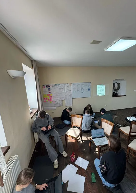 Perspective of the room from above. Various participants sitting, working on laptops.